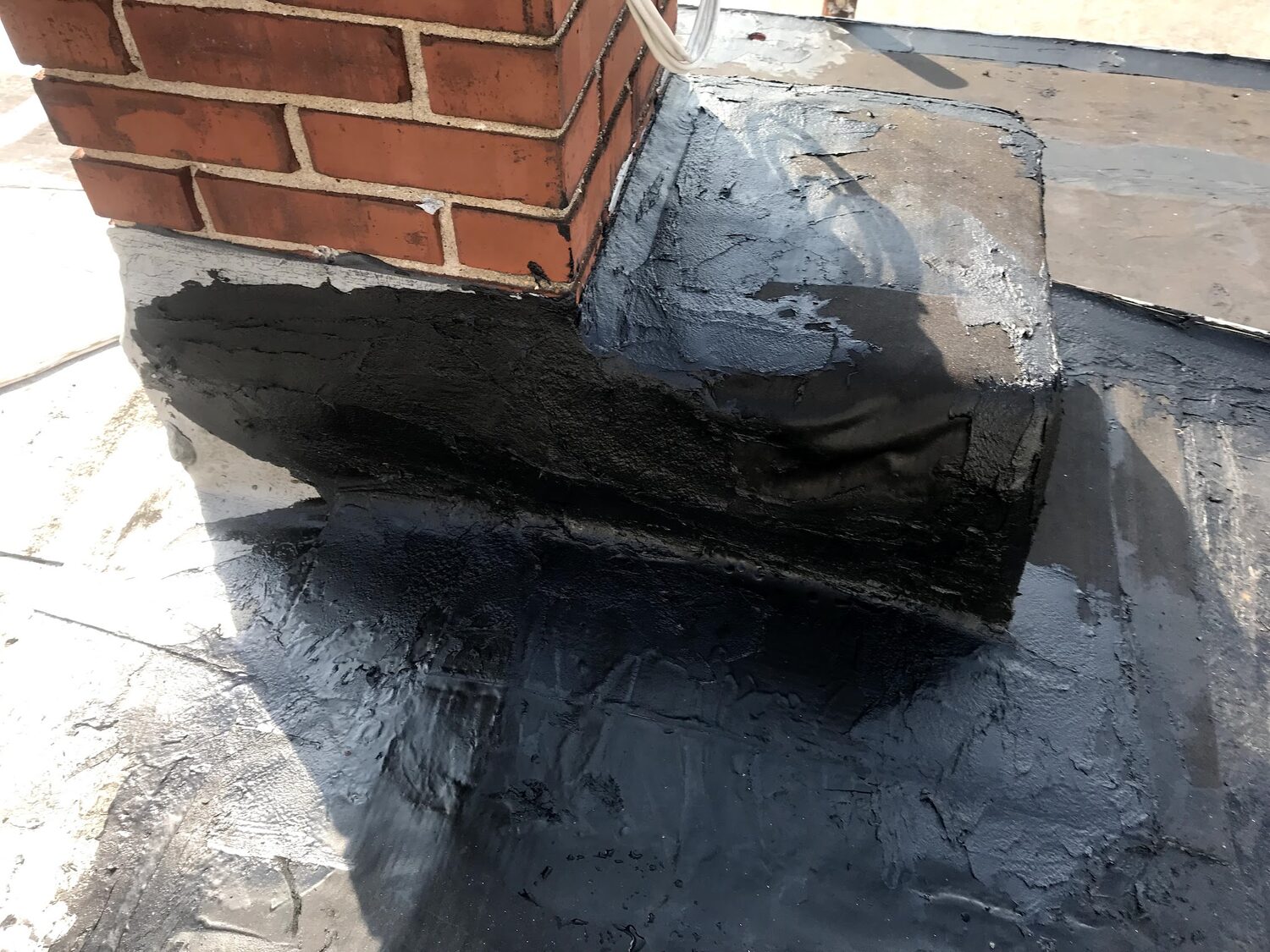 Fresh black flashing sealed where a red brick chimney meets a flat roof